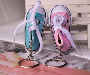 Mini canvas shoe keychains in blue and pink on a white bench prop with macro details