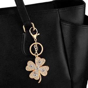 Golden clover keychain with shimmering crystals hanging on a premium black leather handbag