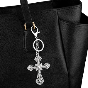 Sparkling cross keychain with silver metal and crystals on a black leather bag