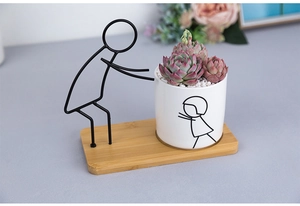 Close-up of minimalist black iron figurine pushing a ceramic succulent pot on wood base