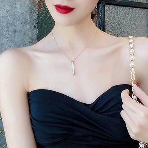 Close-up of a rose gold shell bar pendant necklace worn by a model in soft lighting