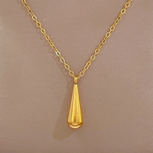 Detail of a minimalist gold teardrop pendant on a sleek titanium steel chain necklace