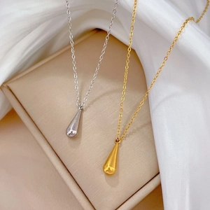 Minimalist gold and silver teardrop pendant necklaces on silk fabric background