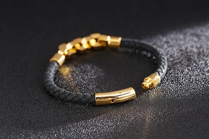 Macro detail of black braided leather bracelet with golden chain links and magnetic clasp