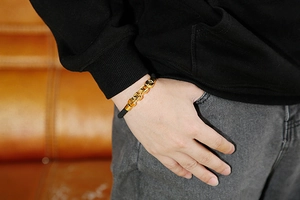 Close-up of a men's black braided leather bracelet with golden chain links on wrist