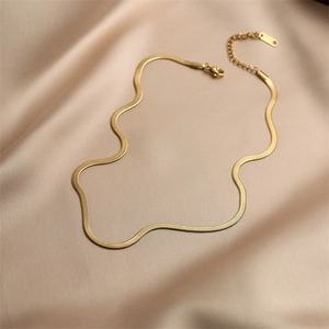 Close-up of golden flat snake chain necklace with lobster clasp on luxury satin fabric
