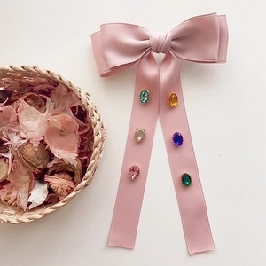 Pink satin bow hair clip with colorful gemstones and streamers on a white background