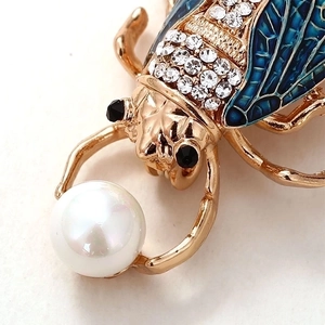 Detailed macro shot of beetle brooch with blue enamel wings and a white pearl