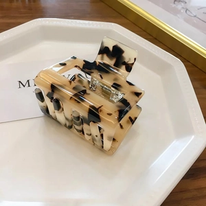Close-up of a large tortoiseshell hair claw clip displayed on a white ceramic tray
