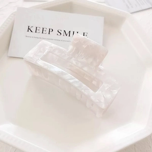 Detail of a large cream rectangle hair claw clip with elegant marble texture on a tray