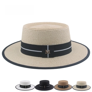 Detail of straw boater hat featuring wide black ribbon and golden metallic M letter buckle