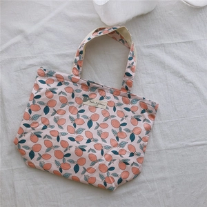 Détail d'un cabas en toile rose à motifs de fruits orange et étiquette en tissu