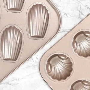 Champagne gold non-stick Madeleine and shell-shaped baking pans on white marble surface