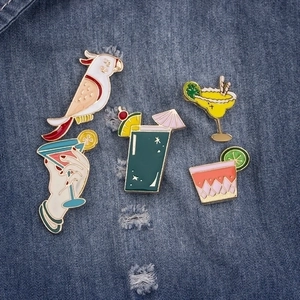 Detail of five enamel pins featuring summer drinks and parrots on denim fabric