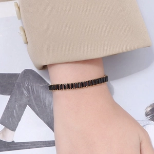 Detail of a 6mm gold tennis bracelet with rectangular black zircons on a model's wrist