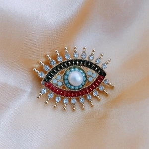 Macro view of evil eye brooch with pearl and colorful crystals on satin background