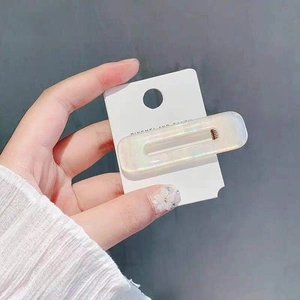 Close-up of a white pearlescent rectangular hair clip on a minimalist display card