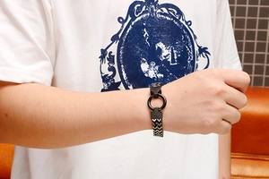 Detail of a men's woven stainless steel bracelet with a black circular ring clasp