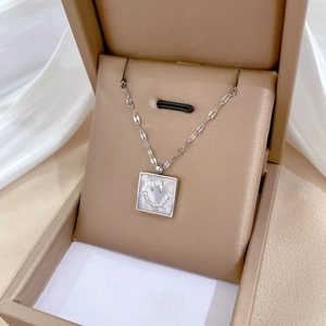 Macro shot of a silver square pendant with a shell inlay and smiley face in a gift box