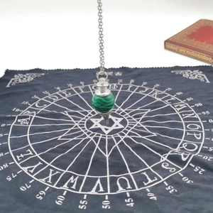 Detail of malachite stone pendulum hanging over a mystical black astrology chart cloth