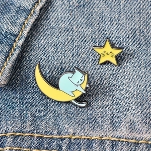 Close-up of cat moon and star enamel pins pinned on dark blue denim fabric