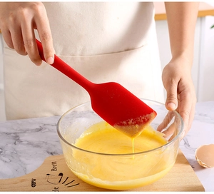Action shot of red silicone spatula mixing egg liquid in a glass bowl in a kitchen