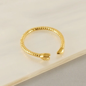 Detail of gold snake ring with scale texture on white stone and grey fabric