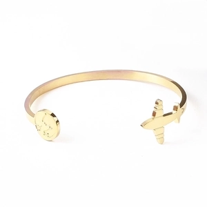 Detailed macro of gold C-shape steel bangle featuring airplane and world map engraving