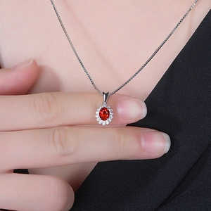 Close-up of a silver necklace featuring a red oval gemstone pendant on a model's neck