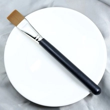Detailed macro view of a professional flat makeup brush with synthetic bristles on white plate
