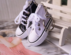 Miniature canvas shoe keychains in black and white displayed on a small white wooden bench