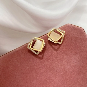 Détail macro de boucles d'oreilles carrées dorées avec œil de chat sur boîte en cuir