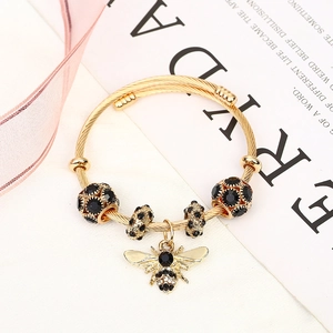 Detail of a gold bee pendant and black rhinestone beads on a steel wire bracelet
