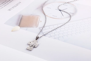 Macro detail of a silver Jesus portrait cross pendant on a minimalist office background