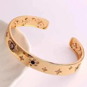 Dettaglio di un bracciale aperto dorato con motivi neri e stelle in zirconia