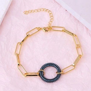 Detail of gold linked bracelet with a black circular pendant and blue crystal pavé accents