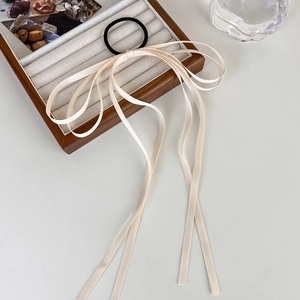Close-up of cream satin bow hair tie with long ribbons on a wooden display tray