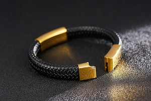 Detail of black braided leather bracelet with gold magnetic clasp on grey background