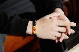 Close-up of a woven black leather medical alert bracelet with a gold Star of Life tag