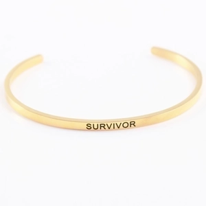 Detail of golden stainless steel mantra bracelet with Survivor engraved lettering