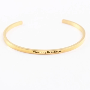 Close-up of gold stainless steel bangle with engraved You Only Live Once quote