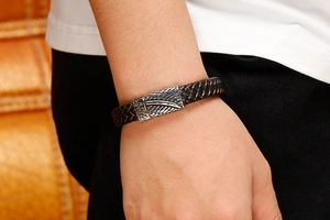 Detail of men's black woven leather bracelet with antique silver feather charm on wrist