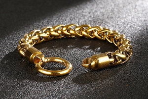 Détail macro du bracelet chaîne dorée polie avec un fermoir rond industriel robuste en métal