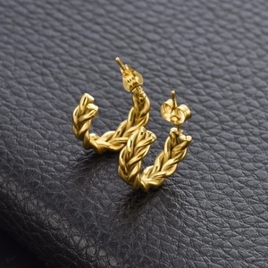 Macro shot of gold twisted rope hoop earrings on premium black textured leather background