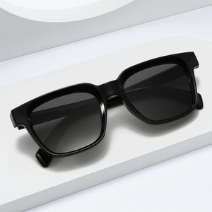 Modern square thick frame sunglasses with grey gradient lenses on a white display stand