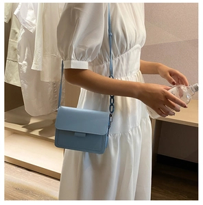 Detail view of a light blue leather square bag with chain strap on white dress