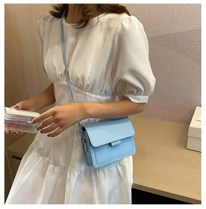 Detailed view of light blue leather crossbody square bag on model in white dress
