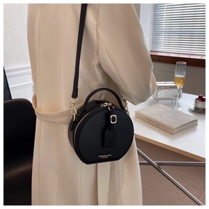Detail of a black leather circular crossbody bag showing the handle and shoulder strap