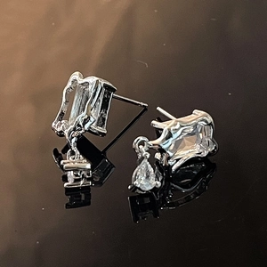 Macro shot of silver butterfly zircon earrings with teardrop pendant on black mirror