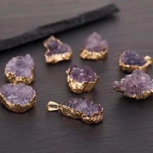 Natural purple amethyst raw stone pendant with gold-plated edge on dark stone surface